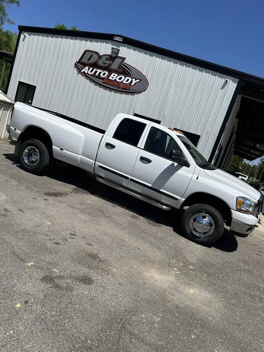 White Dodge Ram 3500 dually crew cab parked in front of the shop under the D&L Auto Body sign